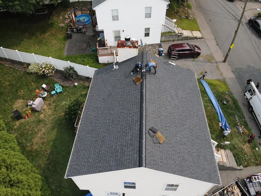 Wide view of the asphalt shingle roof repair process, showing damaged sections being worked on and newly installed shingles blending with the existing roof.