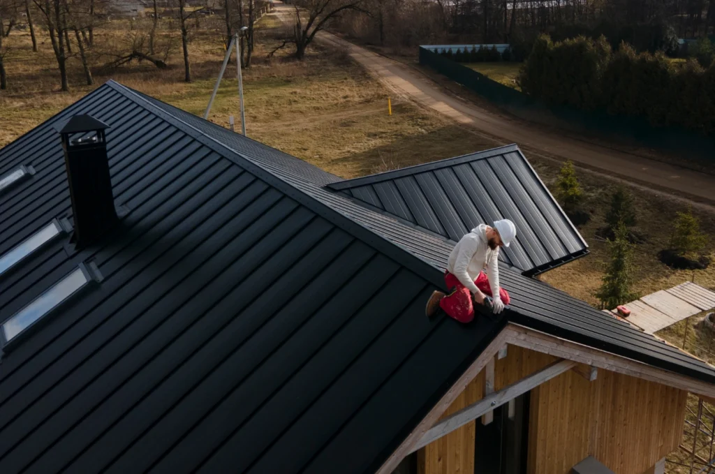 A roofer performing a roof inspection on a standing seam metal roof to check seams, flashing, and other areas that may need attention