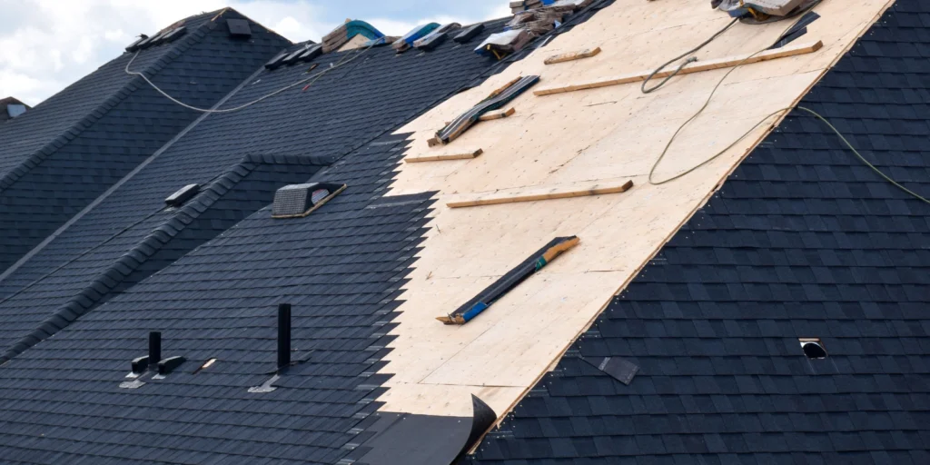 Residential roof under construction with new decking and shingles being installed during a complete roof repair