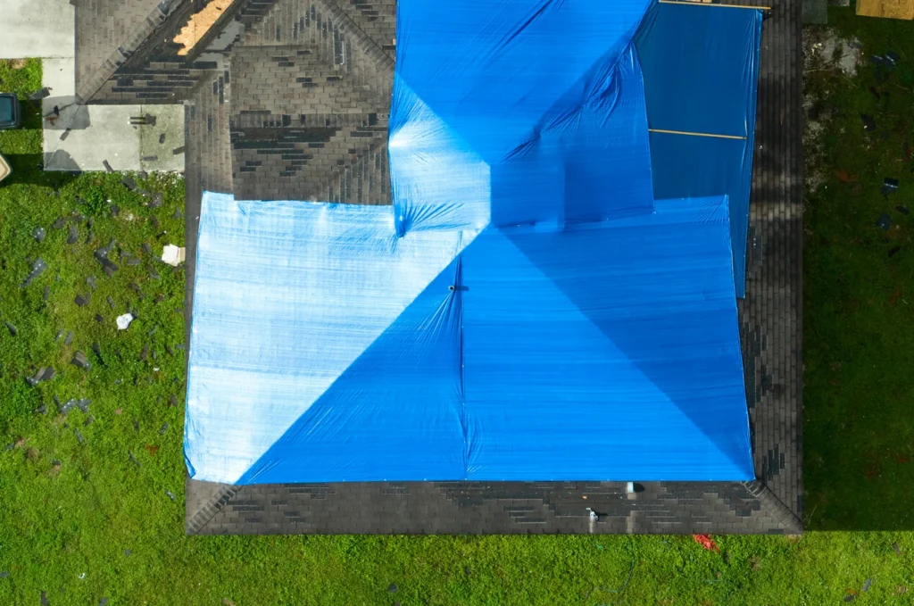 Blue tarp covers damaged roof after emergency roof leak repair planning to help keep homeowners off unsafe wet surfaces. 