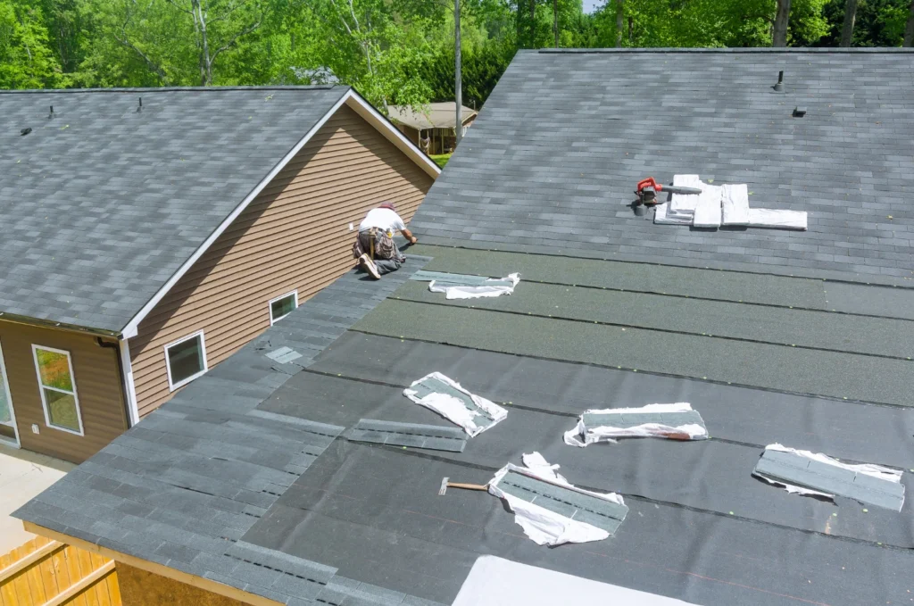 Roofer repairs asphalt shingles on a home roof after early roof damage signs show the need for urgent roof repairs soon. 