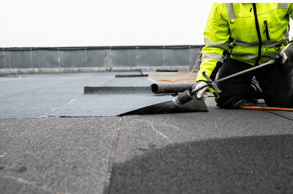 Roofer seals flat roof membrane with a torch during flat roof leak repair service for a Boston commercial property roof.