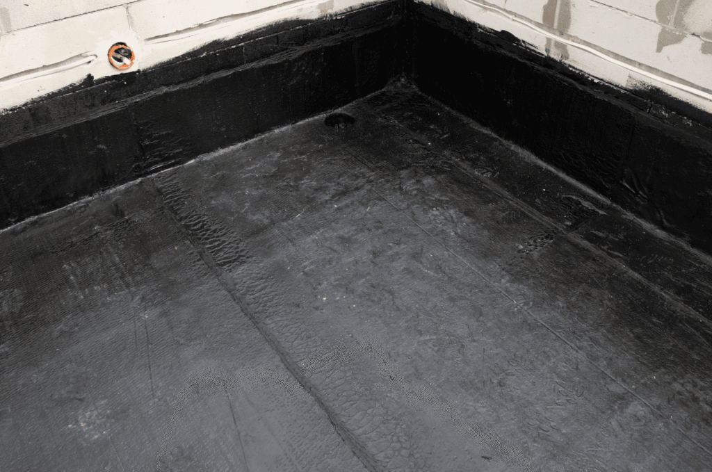 Flat roof with black bitumen waterproofing membrane, parapet wall, and drain outlet linked to early flat roof leak detection