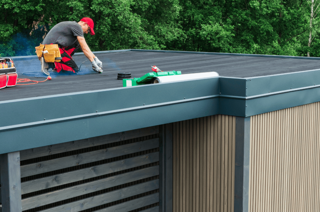 Worker reviews flat roof membrane and drainage areas during maintenance to identify common flat roof problems in Boston.