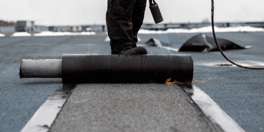 Roofer applies rolled roofing with torch during flat roof repair Boston service for a commercial property with membrane work.