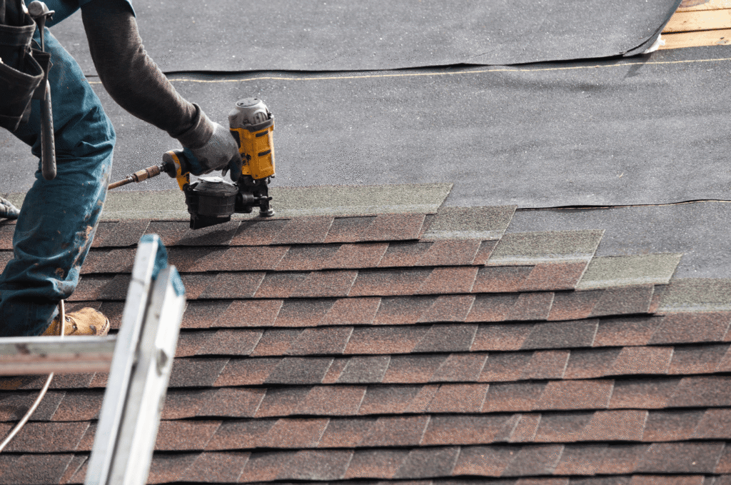 Roofer installs new shingles during residential roof replacement service for a Boston home with older worn roofing materials.